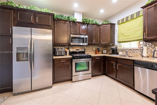 kitchen with dark brown cabinets, light stone countertops, decorative backsplash, and stainless steel appliances