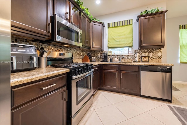 kitchen featuring dark brown cabinetry, light tile patterned floors, stainless steel appliances, and tasteful backsplash