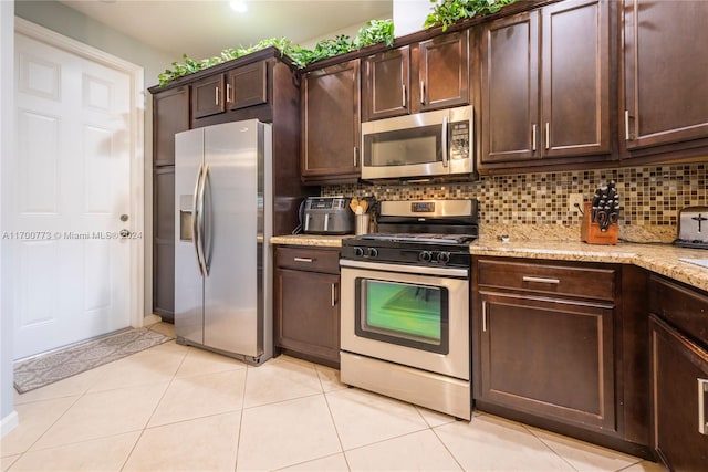 kitchen featuring light stone countertops, appliances with stainless steel finishes, dark brown cabinetry, and backsplash