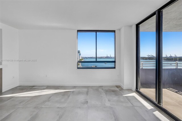 spare room with light wood-type flooring, a water view, and a wall of windows