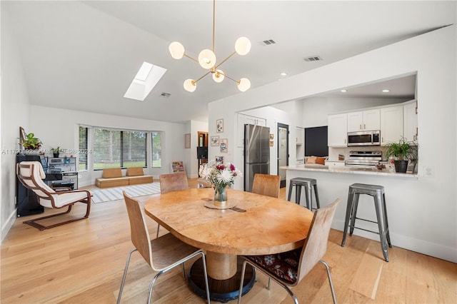 dining space featuring vaulted ceiling with skylight, a notable chandelier, and light hardwood / wood-style flooring