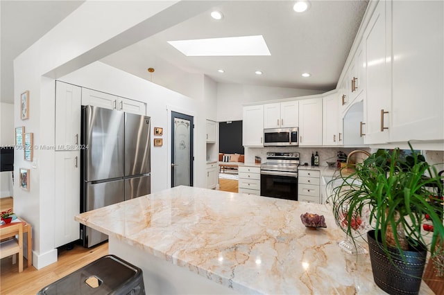 kitchen featuring kitchen peninsula, light stone counters, stainless steel appliances, lofted ceiling with skylight, and white cabinets