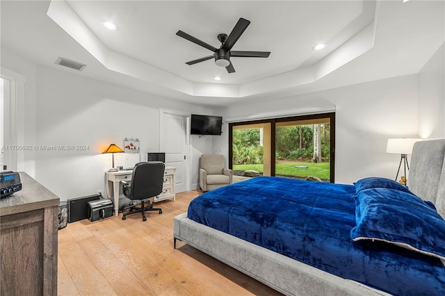 bedroom with ceiling fan, light hardwood / wood-style floors, access to outside, and a tray ceiling