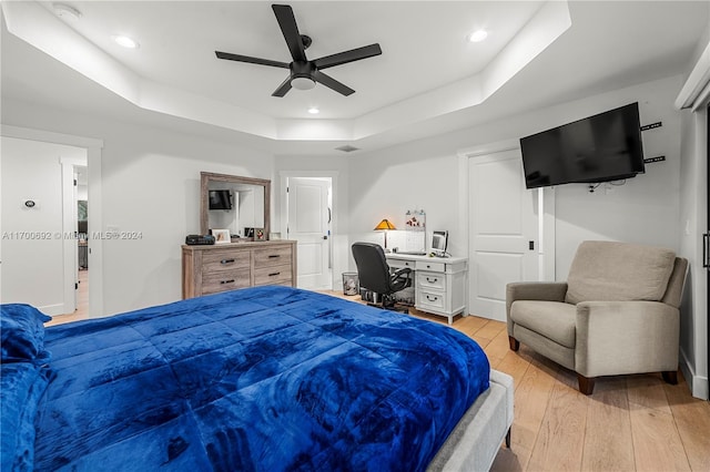 bedroom featuring ceiling fan, a raised ceiling, and light hardwood / wood-style flooring