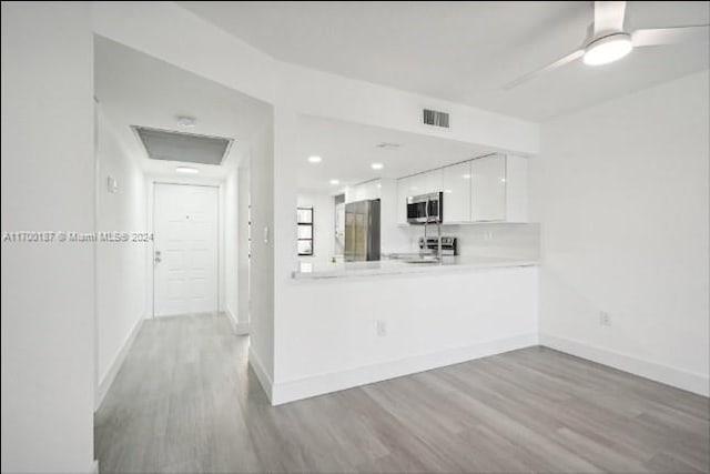 kitchen with white cabinets, appliances with stainless steel finishes, kitchen peninsula, and light hardwood / wood-style flooring