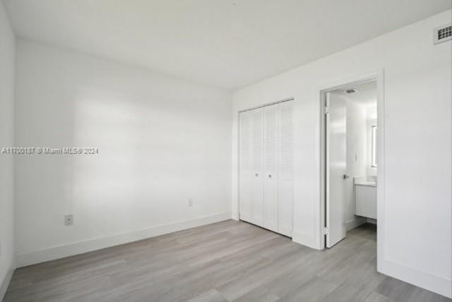 unfurnished bedroom featuring ensuite bathroom, light hardwood / wood-style floors, and a closet