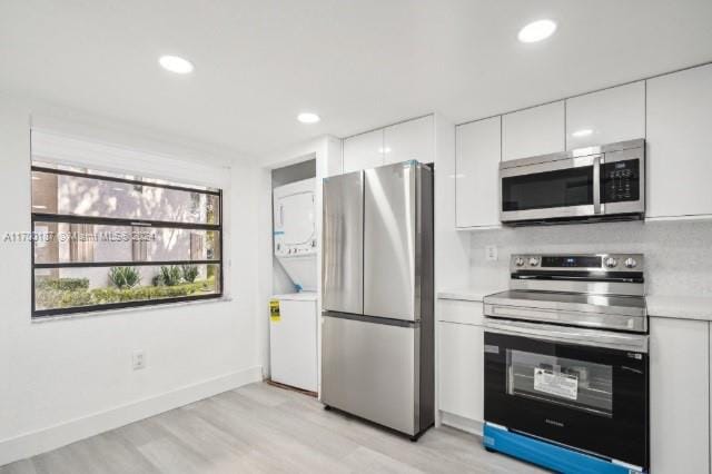 kitchen featuring stacked washer and dryer, stainless steel appliances, white cabinetry, and light hardwood / wood-style flooring