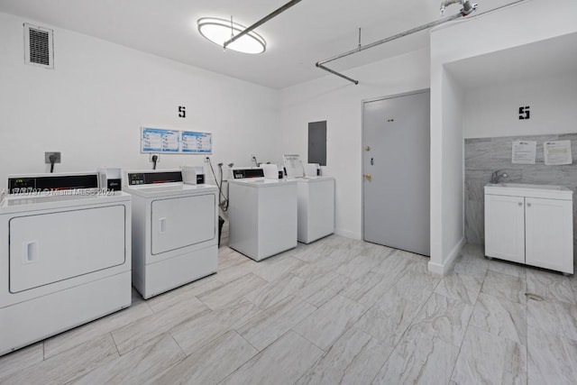 laundry area featuring washer and dryer, electric panel, tile walls, and sink