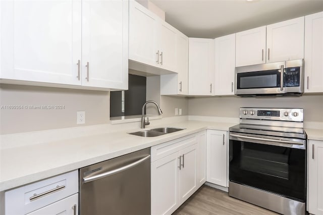 kitchen with appliances with stainless steel finishes, light wood-type flooring, white cabinetry, and sink