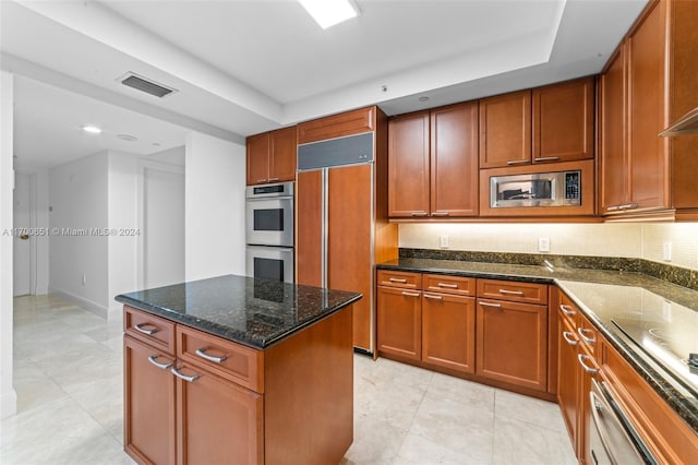 kitchen featuring built in appliances, a center island, light tile patterned flooring, and dark stone counters