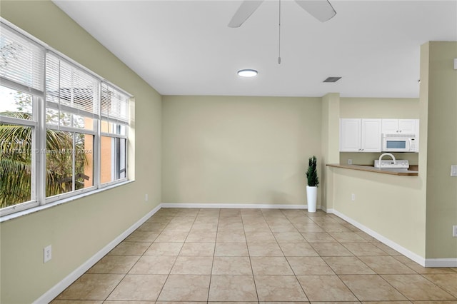 empty room featuring a wealth of natural light, ceiling fan, and light tile patterned flooring