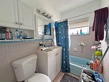 bathroom featuring toilet, tile patterned flooring, shower / tub combo with curtain, and tile walls