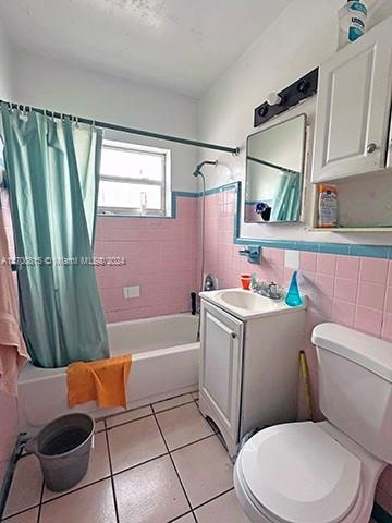 full bathroom with tile patterned flooring, toilet, shower / tub combo with curtain, vanity, and tile walls