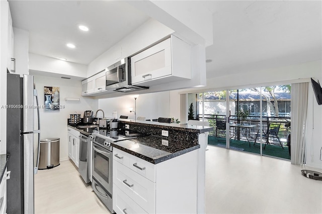 kitchen featuring sink, dark stone countertops, white cabinetry, kitchen peninsula, and stainless steel appliances