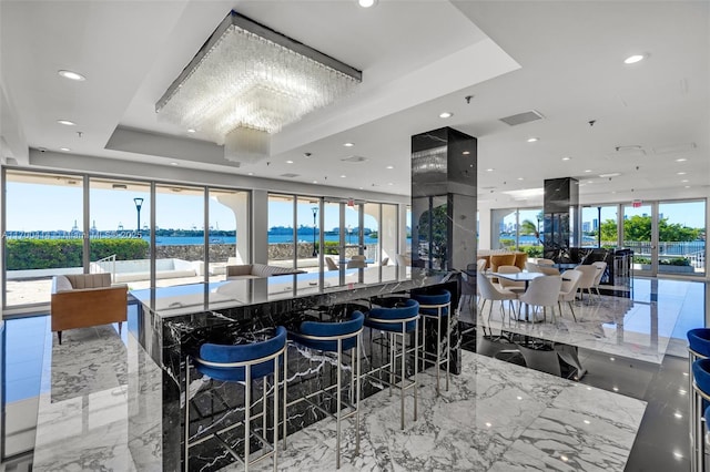 kitchen with a water view, a wealth of natural light, a tray ceiling, a notable chandelier, and a kitchen bar