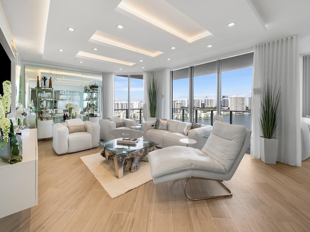 living room with a raised ceiling, light hardwood / wood-style flooring, and a wall of windows