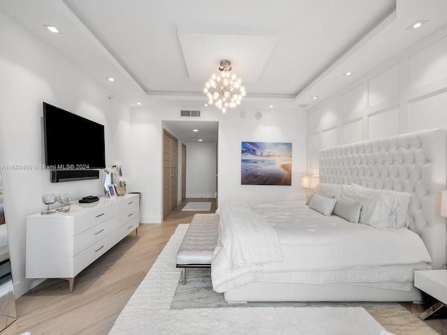 bedroom featuring light hardwood / wood-style floors, an inviting chandelier, and a tray ceiling