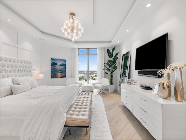 bedroom with a raised ceiling, light hardwood / wood-style flooring, and a chandelier