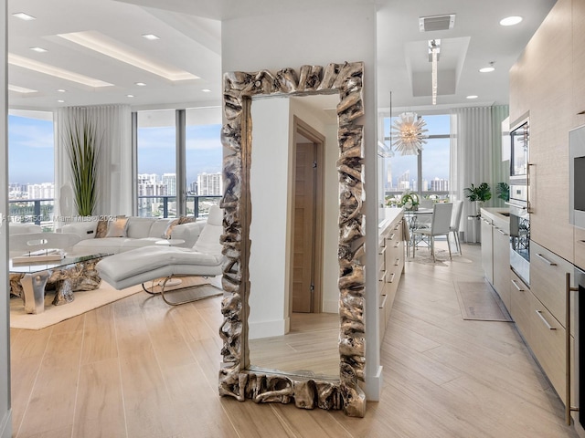 living room featuring a raised ceiling, expansive windows, and light hardwood / wood-style floors