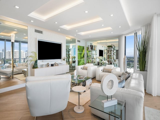 living room featuring plenty of natural light, a raised ceiling, a wall of windows, and light hardwood / wood-style flooring