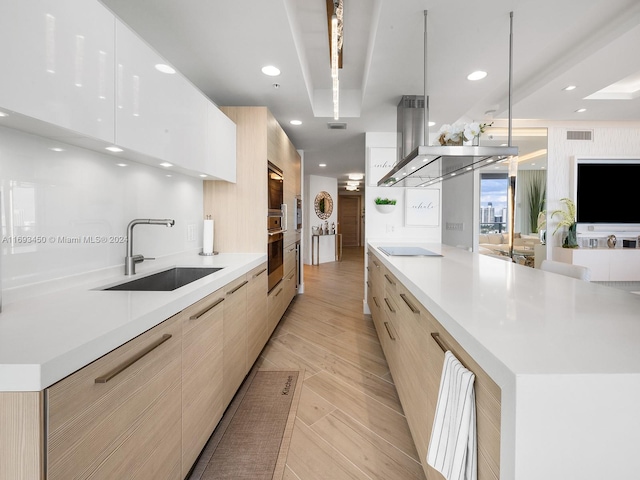 kitchen with black electric stovetop, light wood-type flooring, a large island, and sink