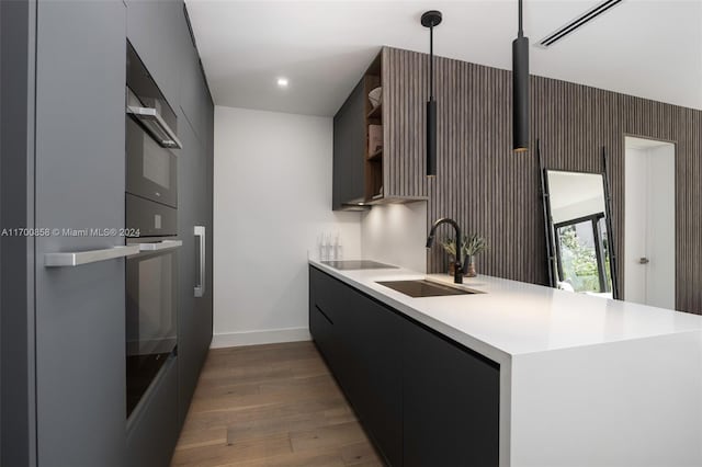 kitchen featuring kitchen peninsula, black electric cooktop, sink, pendant lighting, and dark hardwood / wood-style floors