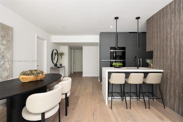 kitchen with double oven, sink, pendant lighting, light hardwood / wood-style flooring, and a breakfast bar area