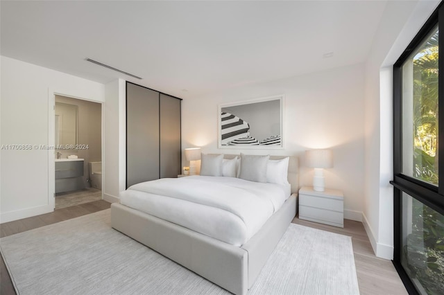 bedroom with light wood-type flooring, ensuite bath, and a closet