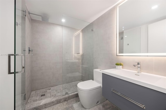 bathroom featuring tasteful backsplash, toilet, vanity, a shower with shower door, and tile walls