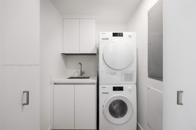 laundry room with cabinets, stacked washing maching and dryer, and sink