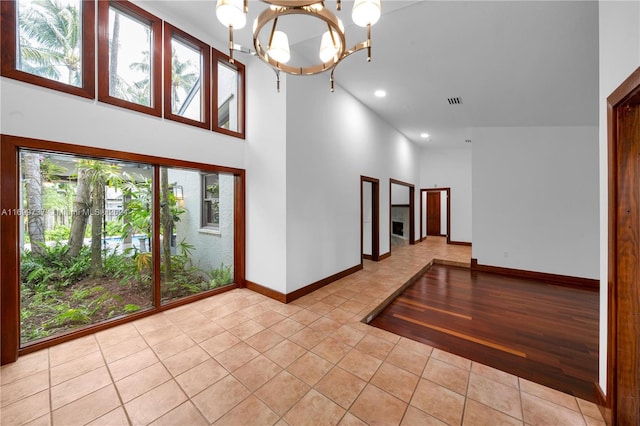 unfurnished room with light hardwood / wood-style flooring, a towering ceiling, and a notable chandelier