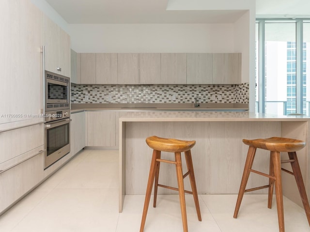 kitchen featuring light tile patterned floors, light brown cabinetry, tasteful backsplash, a kitchen bar, and stainless steel appliances