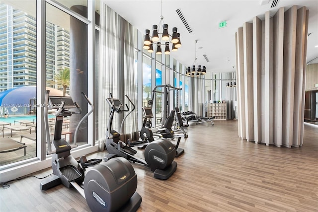 gym with hardwood / wood-style flooring, floor to ceiling windows, a towering ceiling, and a chandelier