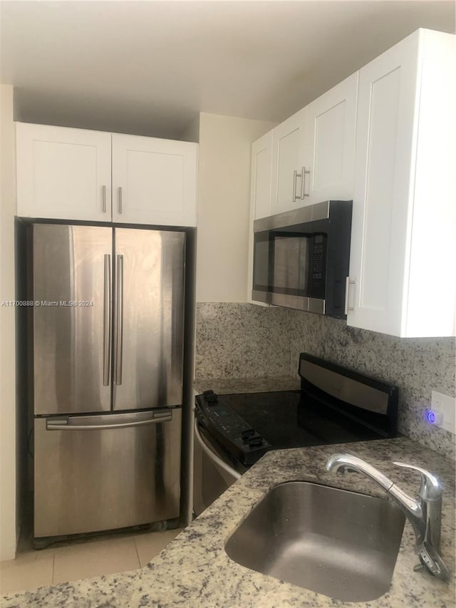 kitchen featuring sink, light stone counters, light tile patterned flooring, white cabinets, and appliances with stainless steel finishes