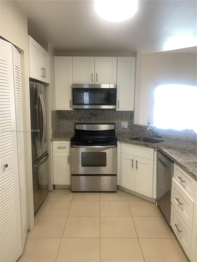 kitchen featuring stainless steel appliances, sink, light tile patterned floors, dark stone countertops, and white cabinetry