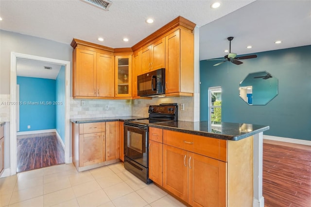 kitchen featuring kitchen peninsula, backsplash, ceiling fan, black appliances, and dark stone countertops