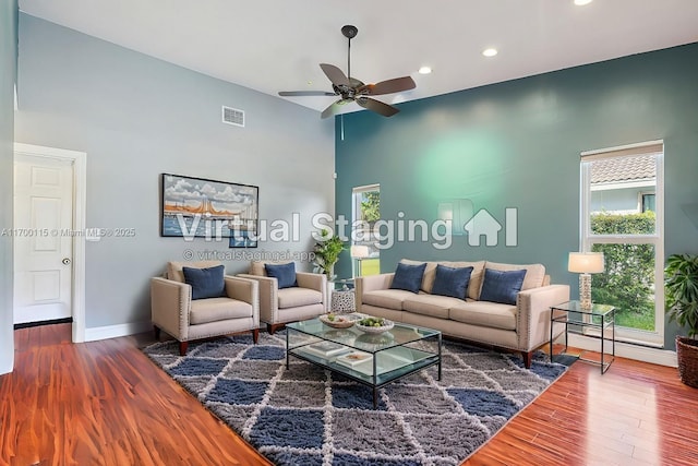 living room featuring ceiling fan, a towering ceiling, and wood-type flooring