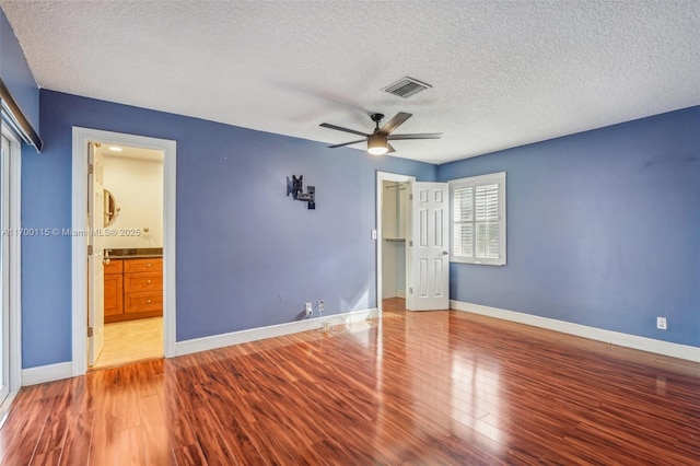 unfurnished bedroom featuring a textured ceiling, ceiling fan, light wood-type flooring, and ensuite bathroom