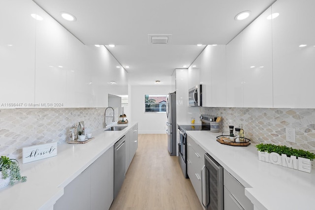 kitchen with appliances with stainless steel finishes, light wood-type flooring, tasteful backsplash, sink, and wine cooler