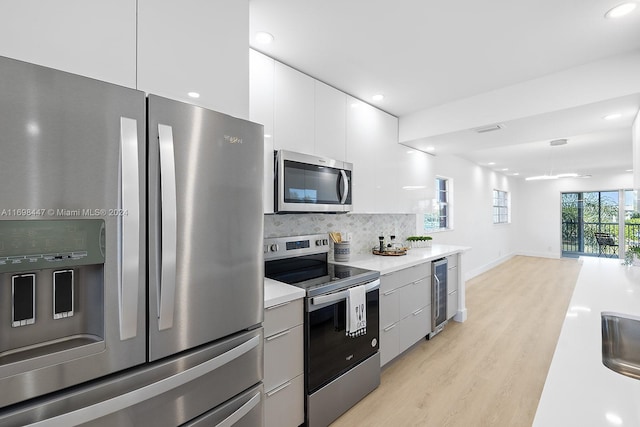 kitchen featuring backsplash, white cabinets, wine cooler, light hardwood / wood-style flooring, and appliances with stainless steel finishes