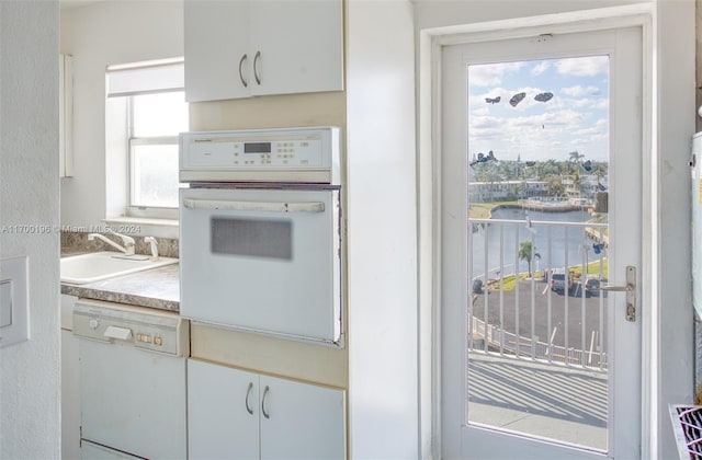 kitchen featuring white cabinets, a water view, white appliances, and sink