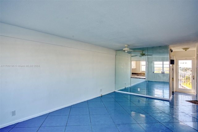 empty room with tile patterned flooring, ceiling fan, and a textured ceiling