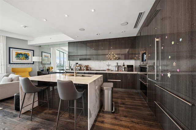 kitchen featuring sink, a kitchen island with sink, tasteful backsplash, dark hardwood / wood-style flooring, and oven