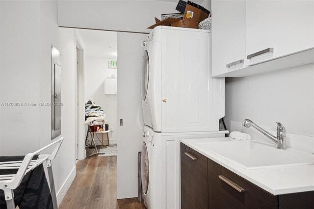 laundry area with cabinets, stacked washer and dryer, dark wood-type flooring, and sink