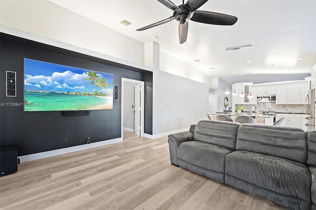 living room with ceiling fan, vaulted ceiling, and light wood-type flooring