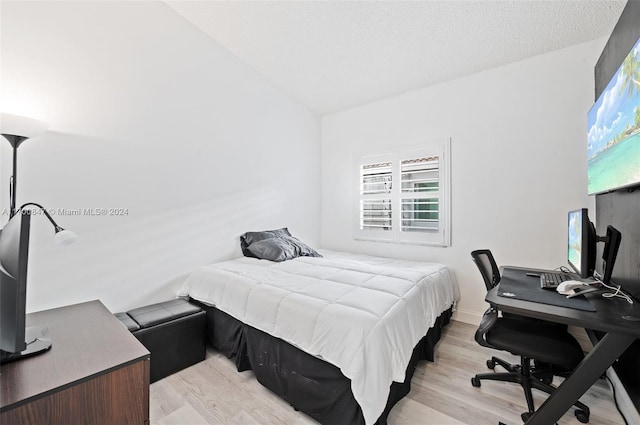 bedroom featuring a textured ceiling, light hardwood / wood-style flooring, and lofted ceiling