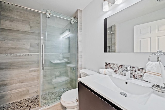 bathroom featuring vanity, toilet, walk in shower, and tasteful backsplash