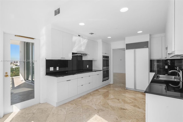 kitchen featuring decorative backsplash, paneled refrigerator, white cabinetry, and sink