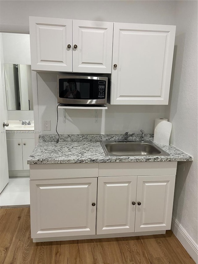 kitchen with white cabinets, light hardwood / wood-style floors, light stone counters, and sink