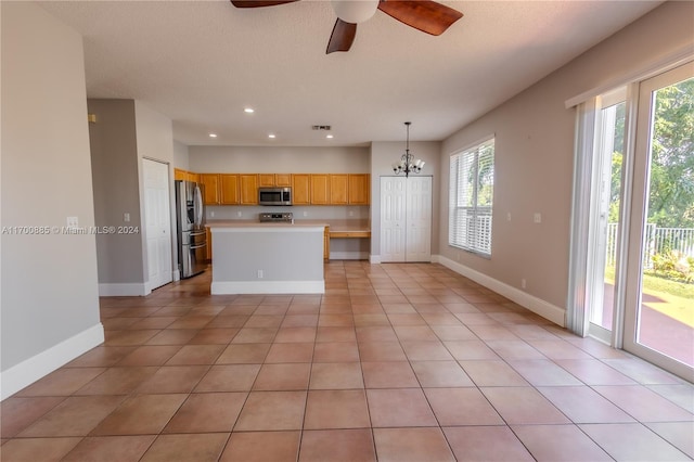 kitchen with decorative light fixtures, stainless steel appliances, a kitchen island, and light tile patterned flooring